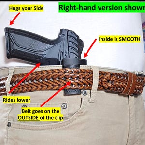 Op de afbeelding: Een zwart pistoolholster wordt getoond, vastgeklikt aan een bruine gevlochten leren riem. De tekst "Right-hand version shown" is zichtbaar. Het holster is ontworpen om lager te zitten en de zijkant te omarmen. De riem gaat aan de buitenkant van de clip.