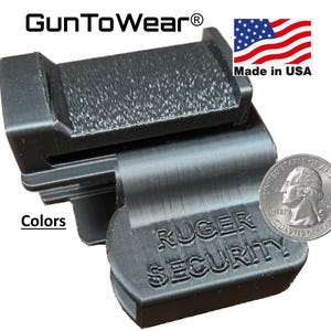 Op de afbeelding: Zwart Ruger Security accessoire met getextureerde oppervlakken. Het product heeft de tekst "Ruger Security" en "Made in USA". Een munt is inbegrepen ter groottevergelijking. Het product is van GunToWear.