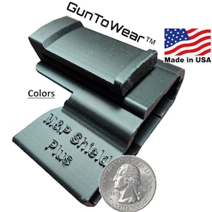 May include: Black polymer M&P Shield Plus magazine holder. The product has the text "Gun To Wear" and "M&P Shield Plus". The American flag and "Made in USA" are also visible. A quarter is included for size reference.