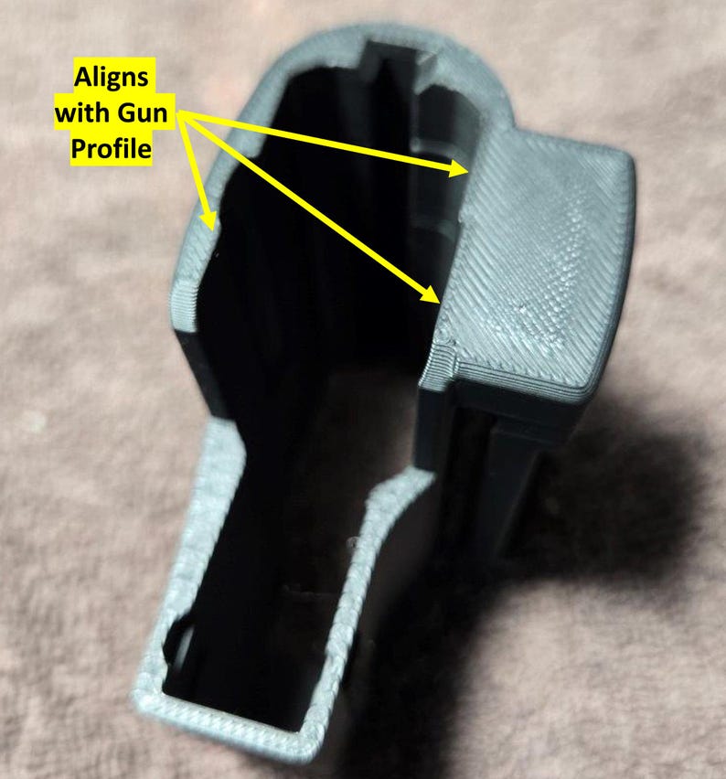 May include: A gray 3D-printed object with the text "Aligns with Gun Profile" and yellow arrows pointing to the edges. The object has a hollow interior and a textured surface, designed to fit a gun profile.
