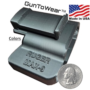 May include: A black holster for a Ruger MAX-9 pistol. The holster is made in the USA and features the text "GunToWear" and "RUGER MAX-9". A US quarter is included for size comparison. The word "Colors" is also visible.