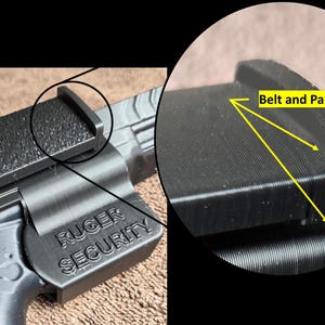 Op de afbeelding: Zwart Ruger Security accessoire met een getextureerde grip en de woorden "Ruger Security" in reli&euml;f aan de zijkant. De afbeelding toont ook een close-up van het "Belt and Pants Grip" gebied.