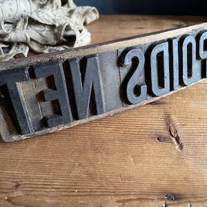 May include: A vintage wooden printing block with the text "NET 20109" in bold, black letters. The block is rectangular and rests on a wooden surface. The letters are raised and appear to be made of metal.