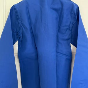 Op de afbeelding: Een effen blauw, lang mouwig werkshirt met een knoopsluiting en een kraag.