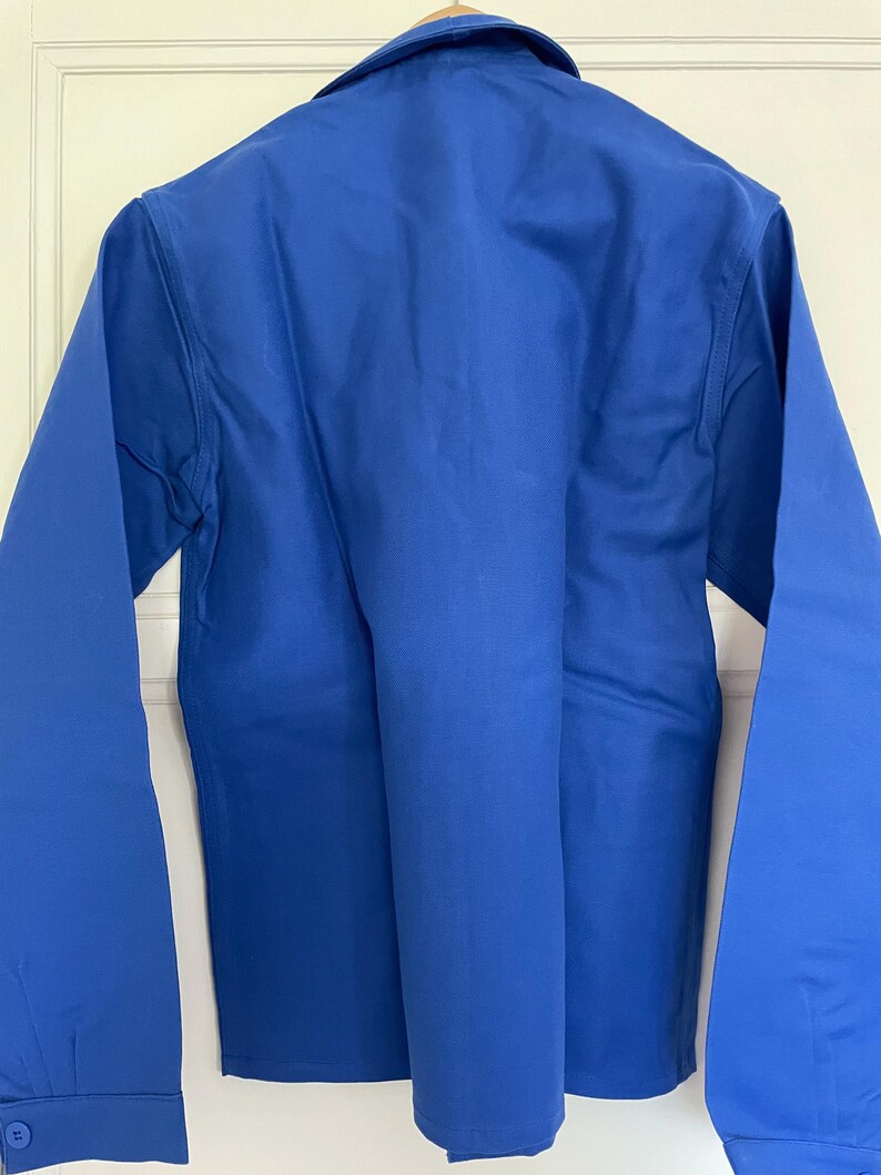 Op de afbeelding: Een effen blauw, lang mouwig werkshirt met een knoopsluiting en een kraag.