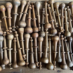 Op de afbeelding: Een verzameling houten spoelen in verschillende vormen en maten, in tinten bruin en beige. De natuurlijke houtnerf is zichtbaar op elke spoel. Sommige hebben een donkerdere vlek. De spoelen zijn dicht bij elkaar geplaatst.
