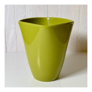 May include: A glossy, lime green ceramic vase with a unique, angular design. The vase has a square top and a gently tapered body. The smooth surface reflects light, highlighting the vibrant color. This decorative vase is suitable for displaying flowers or as a standalone accent piece.