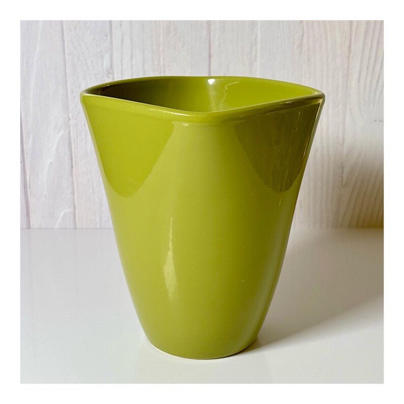 May include: A glossy, lime green ceramic vase with a unique, angular design. The vase has a square top and a gently tapered body. The smooth surface reflects light, highlighting the vibrant color. This decorative vase is suitable for displaying flowers or as a standalone accent piece.