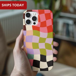 Puede incluir: Una funda de teléfono colorida con un patrón de tablero de ajedrez en tonos de rojo, rosa, verde, morado y negro. La funda se sostiene en una mano y tiene un recorte para la cámara. El texto "SHIPS TODAY" está en un rectángulo rojo en la parte superior.