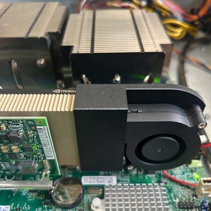 May include: A green circuit board featuring an NVIDIA graphics card with a black blower-style cooling fan and a metallic heatsink. The board includes an Intel chip, a circular battery, a Lattice processor, and various silver metallic components.