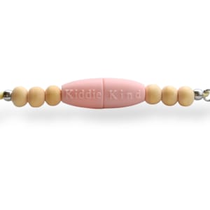 May include: A baby pink pacifier clip with the text "Kiddie Kind" in the center. The clip features wooden beads and a silver chain. The clip is designed to attach to a pacifier.
