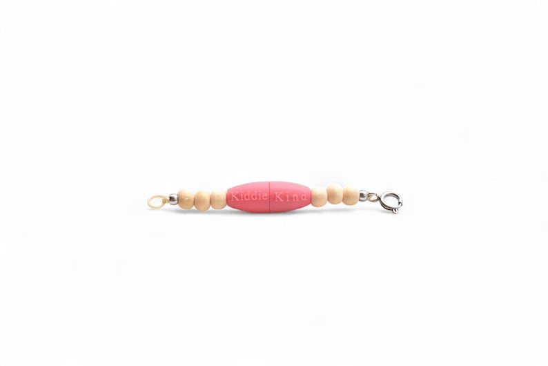 May include: A baby teething necklace with a pink, oval-shaped silicone bead in the center, flanked by small, light-colored wooden beads. The text "Kiddie King" is printed on the pink bead. The necklace has a clasp closure.