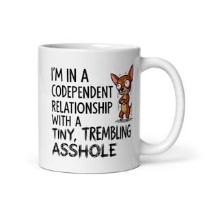 May include: White ceramic mug featuring the text "I'M IN A CODEPENDENT RELATIONSHIP WITH A TINY, TREMBLING ASSHOLE" and a cartoon chihuahua. The mug has a white handle and a glossy finish.