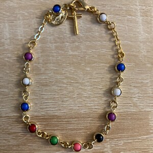 May include: Gold-coloured bracelet with a series of colourful, round beads. The bracelet includes a small gold cross charm and a medallion. The beads are in various colours, including blue, red, green, and pink.