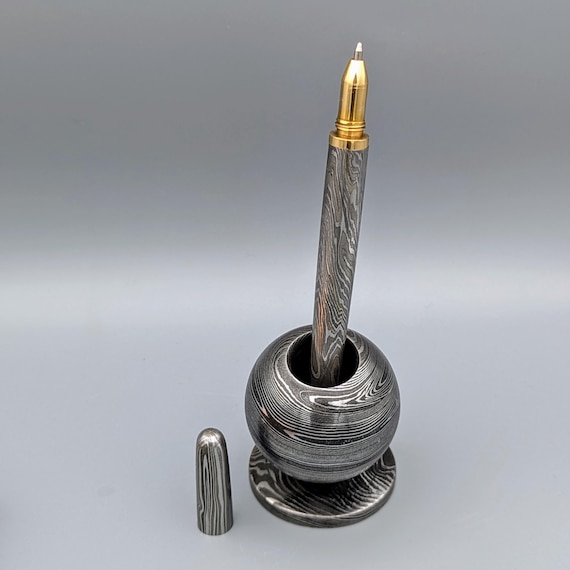 A fully functional writing pen forged from Damascus steel — the same swirling, layered metal used in legendary blades — giving a desk tool an almost mythological edge.