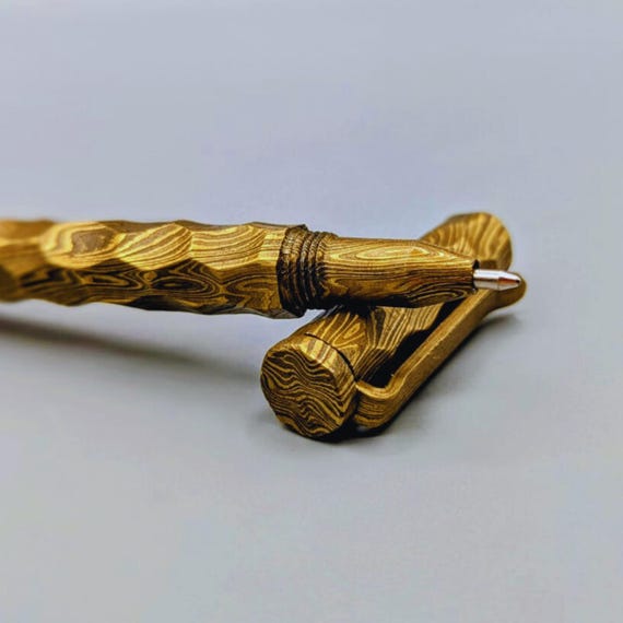 Gold-tinted Damascus steel twisted into a ballpoint pen, shipped in a custom-engraved wooden box — a writing instrument that stops people mid-meeting.