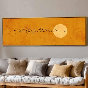 Puede incluir: Obra de arte rectangular enmarcada en dorado. La imagen muestra un fondo amarillo-naranja, un gran sol blanco y una bandada de pájaros negros en silueta. Una pieza decorativa.