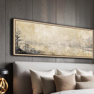 Könnte beinhalten: Ein rechteckiges Landschaftsgemälde mit hellem Holzrahmen hängt über einem Bett. Das Kunstwerk zeigt eine neblige Szene mit Bäumen und Bergen in gedämpften Tönen von Beige, Grau und Schwarz. Das Gemälde ist an einer dunkelgrauen Wand mit Paneelen angebracht.