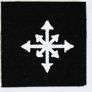 Op de afbeelding: Een zwarte stoffen patch met een wit achtpuntig sterontwerp. De ster is gemaakt van acht pijlen die in verschillende richtingen wijzen.