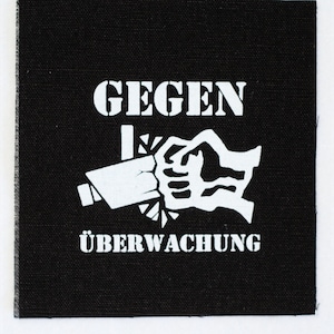 May include: Black and white patch with the text "GEGEN ÜBERWACHUNG" and a graphic of a fist crushing a surveillance camera.