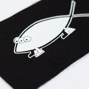 May include: A black patch with a white outline of a fish with three eyes and legs. The fish is in the shape of a Christian fish symbol.