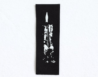 May include: A white candle with a flame on a black fabric background.