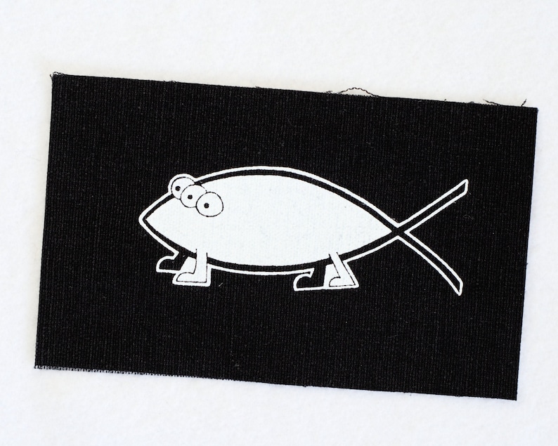 May include: A black fabric patch with a white outline of a fish with three eyes and legs. The fish is walking on its legs.