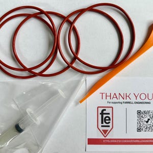 May include: An assortment of automotive repair parts, including four red O-rings, an orange plastic tool, and a syringe filled with a white substance. A thank you card with the Farrell Engineering logo is also included.