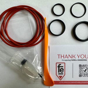 May include: An assortment of black rubber rings, red rubber rings, an orange tool, and a syringe are displayed on a white surface. A card with the text "THANK YOU!" and the Farrell Engineering logo is also present.