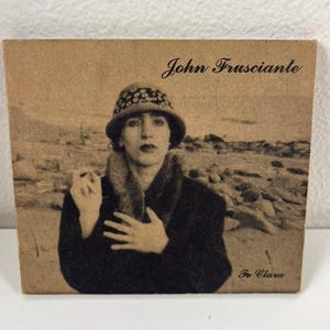 May include: A sepia-toned album cover featuring a woman in a cloche hat and fur-trimmed coat. The text "John Frusciante" is at the top, with "To Clara" at the bottom. The background shows a coastal landscape.
