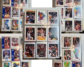 May include: A collection of vintage basketball trading cards in protective sleeves, featuring various players in action poses. The cards are arranged in a binder, showcasing the players and team logos.
