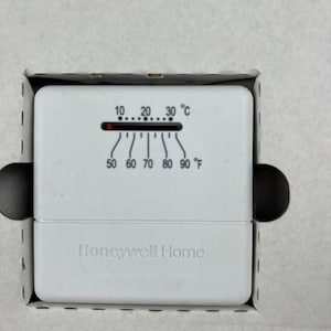 May include: A white Honeywell Home thermostat with temperature scales in Fahrenheit and Celsius. The thermostat is in a cardboard box. The temperature is set to approximately 70 degrees Fahrenheit.