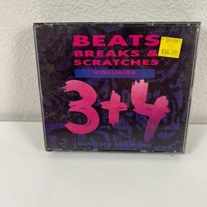 May include: A CD case with the title "BEATS BREAKS & SCRATCHES" in pink and white text. The CD is labeled "VOLUMES 3+4" with the artist's name, Simon Harris, below. The background is a dark purple and black design.
