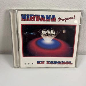 May include: A CD case featuring the Nirvana album. The cover has the band's name in red and blue, with the word "Original" in red. The artwork depicts a red and blue design with a white burst.