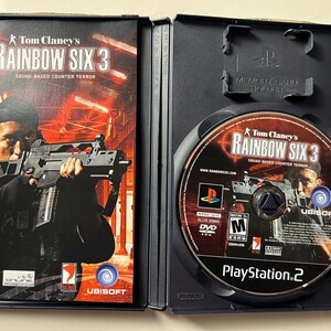 Puede incluir: Caja de juego de PlayStation 2 abierta para Tom Clancy's Rainbow Six 3. La car&aacute;tula presenta a una persona sosteniendo un arma. El disco del juego es visible dentro de la caja.