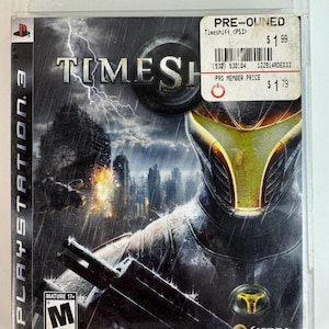 May include: A PlayStation 3 video game case for the game Timeshift. The cover art features a futuristic character in a dark suit and yellow-tinted helmet, a stormy cityscape with a clock tower, and a white price sticker in the upper right corner.