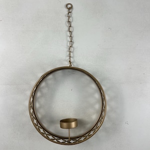 May include: A gold-toned, circular candle holder with a decorative geometric pattern. The candle holder is suspended by a chain and features a small cup to hold a candle. The design is simple and elegant, suitable for home decor.