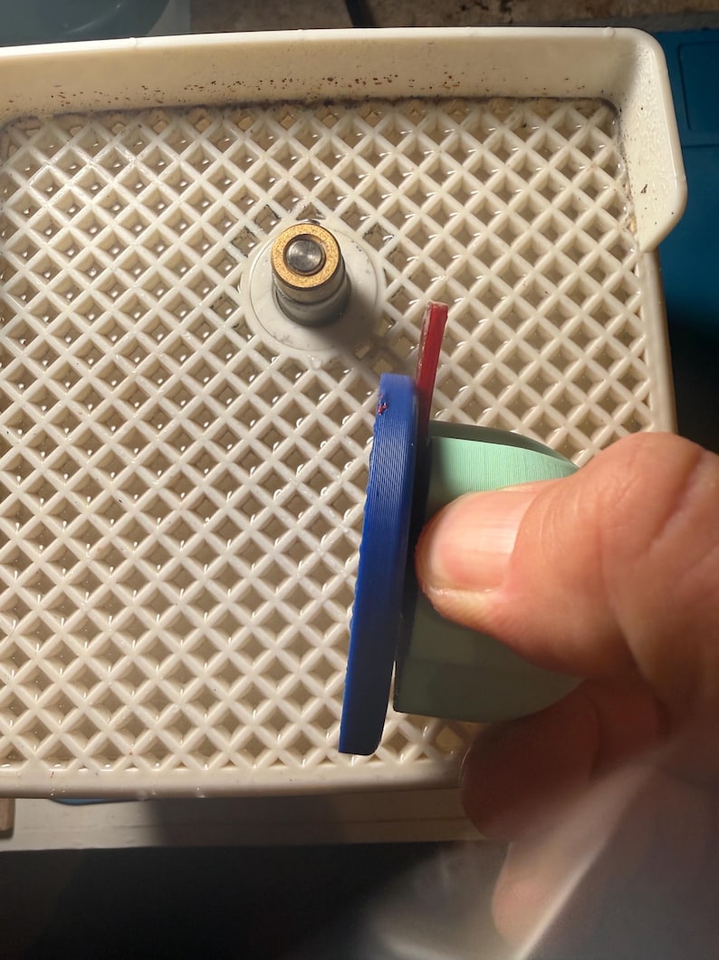 Op de afbeelding: Een close-up van een glassnijgereedschap met een blauwe handgreep en een rood mes. Het gereedschap bevindt zich op een wit plastic rooster. Het gereedschap wordt door een hand vastgehouden.