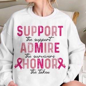Può includere: Felpa bianca con testo rosa che recita "SUPPORT the support, ADMIRE the survivors, HONOR the taken." La parola "SUPPORT" è in un carattere rosa brillante e in grassetto. Le altre parole sono in un carattere rosa più tenue.