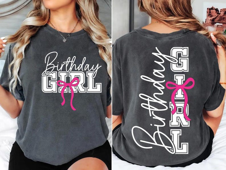 May include: Charcoal gray t-shirt with the words "Birthday GIRL" in white script and block letters, accented with a pink bow. The back of the shirt repeats the design vertically.
