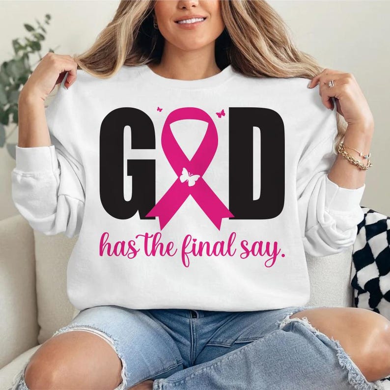 Puede incluir: Sudadera blanca con el texto "GOD" en negro, una cinta rosa y las palabras "has the final say" en rosa. El dise&ntilde;o incluye mariposas. La sudadera la lleva una persona.