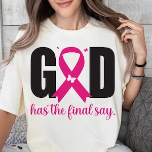 Puede incluir: Camiseta color crema con la palabra "GOD" en letras negras grandes, una cinta rosa y la frase "has the final say". El dise&ntilde;o incluye mariposas rosas. La camiseta es de estilo casual.