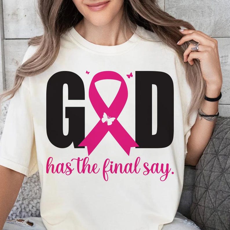 Puede incluir: Camiseta color crema con la palabra "GOD" en letras negras grandes, una cinta rosa y la frase "has the final say". El dise&ntilde;o incluye mariposas rosas. La camiseta es de estilo casual.