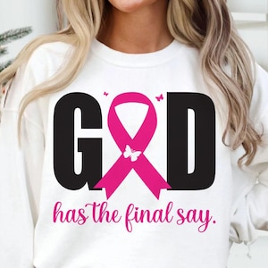 Puede incluir: Sudadera blanca con la palabra "GOD" en letras negras, una cinta rosa y la frase "has the final say" en escritura rosa. Un gr&aacute;fico de mariposa est&aacute; en la cinta.