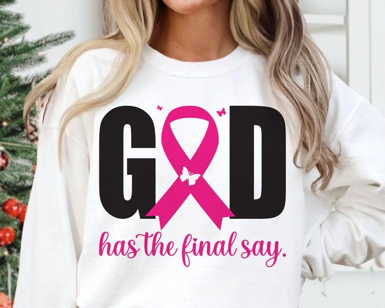 Puede incluir: Sudadera blanca con la palabra "GOD" en letras negras, una cinta rosa y la frase "has the final say" en escritura rosa. Un gr&aacute;fico de mariposa est&aacute; en la cinta.