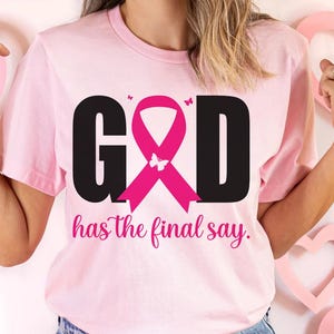 Puede incluir: Camiseta rosa claro con la palabra "GOD" en negro, una cinta rosa y la frase "has the final say" en cursiva. La cinta tiene una mariposa en el centro. Peque&ntilde;as mariposas a ambos lados de la cinta.