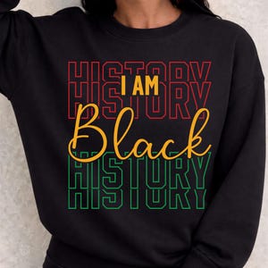 Könnte beinhalten: Schwarzes Sweatshirt mit dem Text "I AM Black HISTORY" in Rot, Gelb und Grün. Das Wort "HISTORY" ist vertikal in einer fetten Schriftart gestapelt. Das Sweatshirt ist schwarz.
