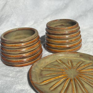 May include: A white ceramic mug with a black handle and the text "But First, Coffee" in a black, bold font. The mug is on a wooden surface. The mug is 10 cm tall.