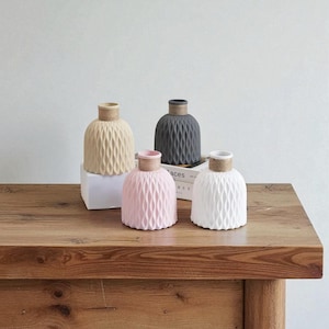Peut inclure: Quatre vases décoratifs en céramique beige, gris, rose et blanc, chacun avec un motif en losange texturé et un accent en ficelle naturelle autour du col. Les vases sont présentés sur une surface en bois, pour la décoration intérieure.
