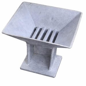 May include: A gray, square-based sculpture with a rectangular top and a slatted interior. The sculpture has a pedestal base and a textured surface. The top is angled, and the overall design is geometric.